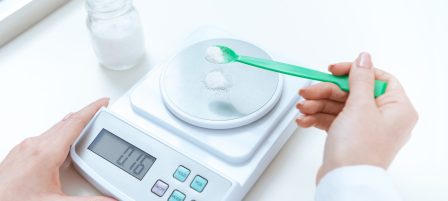 Close-up partial view of chemist weighing reagent on laboratory scales